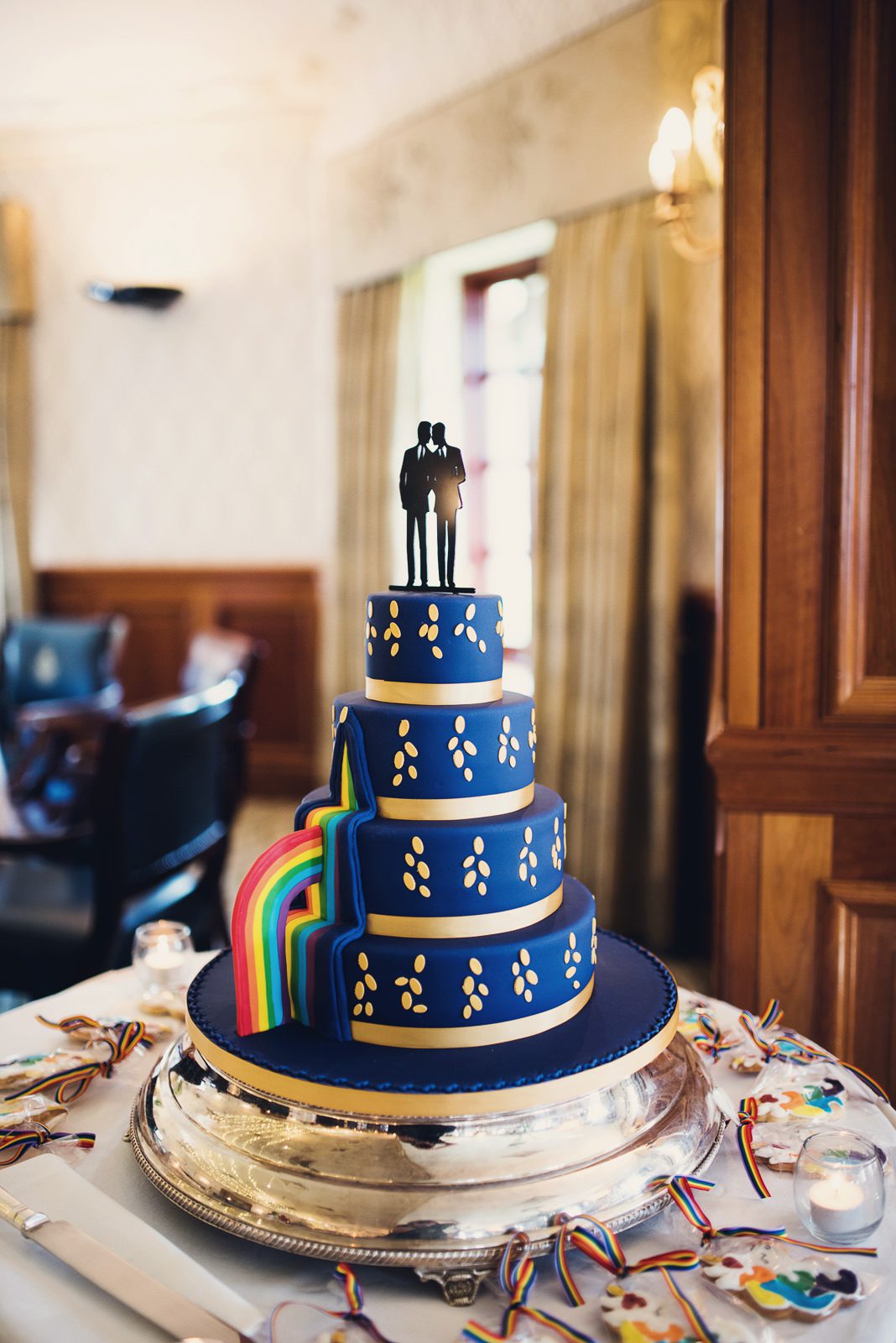 Fabulous blue multi tiered wedding cake for a same sex wedding featuring a rainbow and two grooms silhouette.