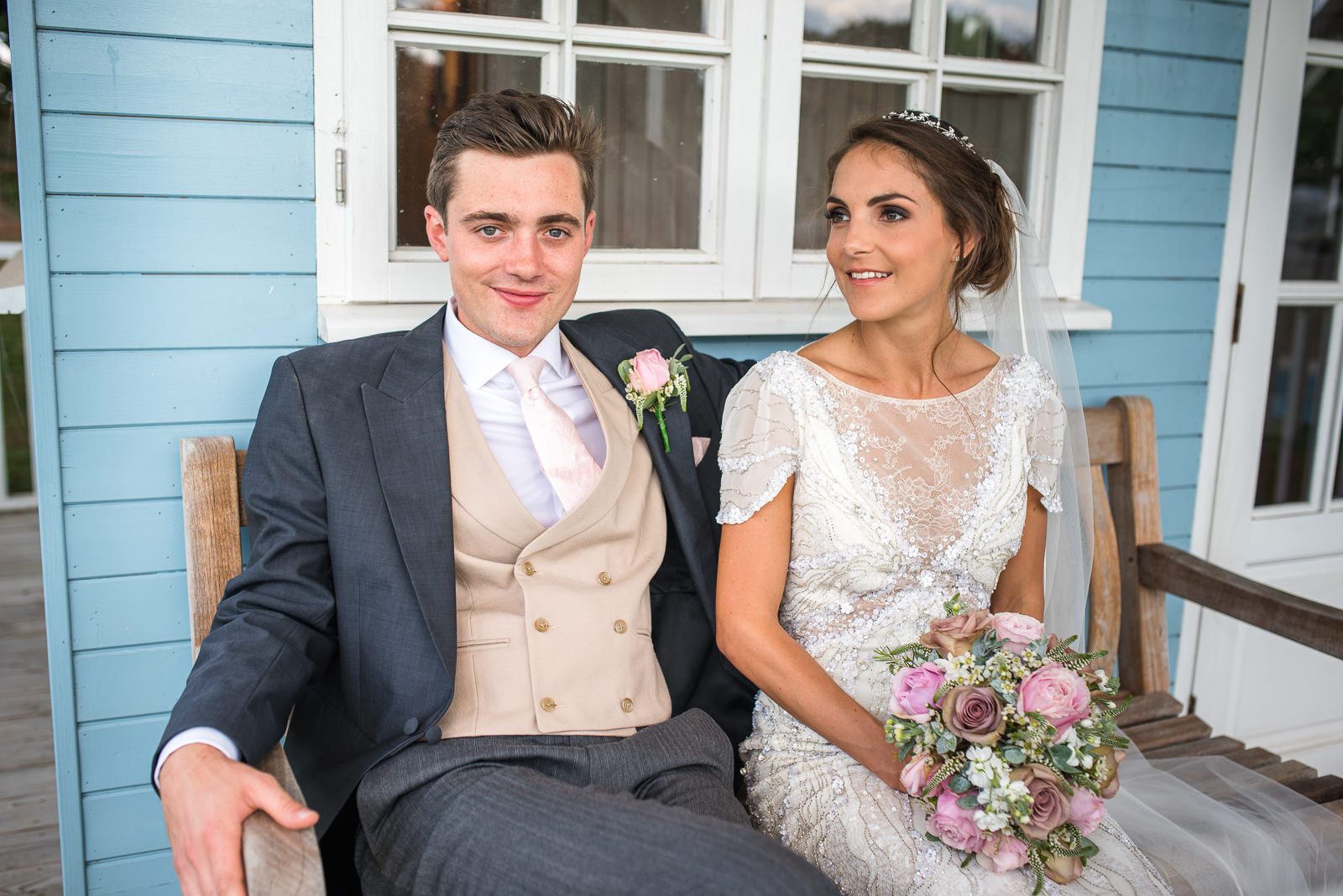 Stylish and beautiful bride and groom photo of the couple sat on a bench in the grounds of the family home.