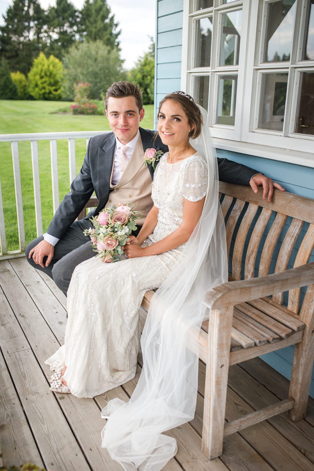 Ideas for bride and groom photographs with a portrait of the bride and groom sitting outside a pastel blue cricket pavilion.