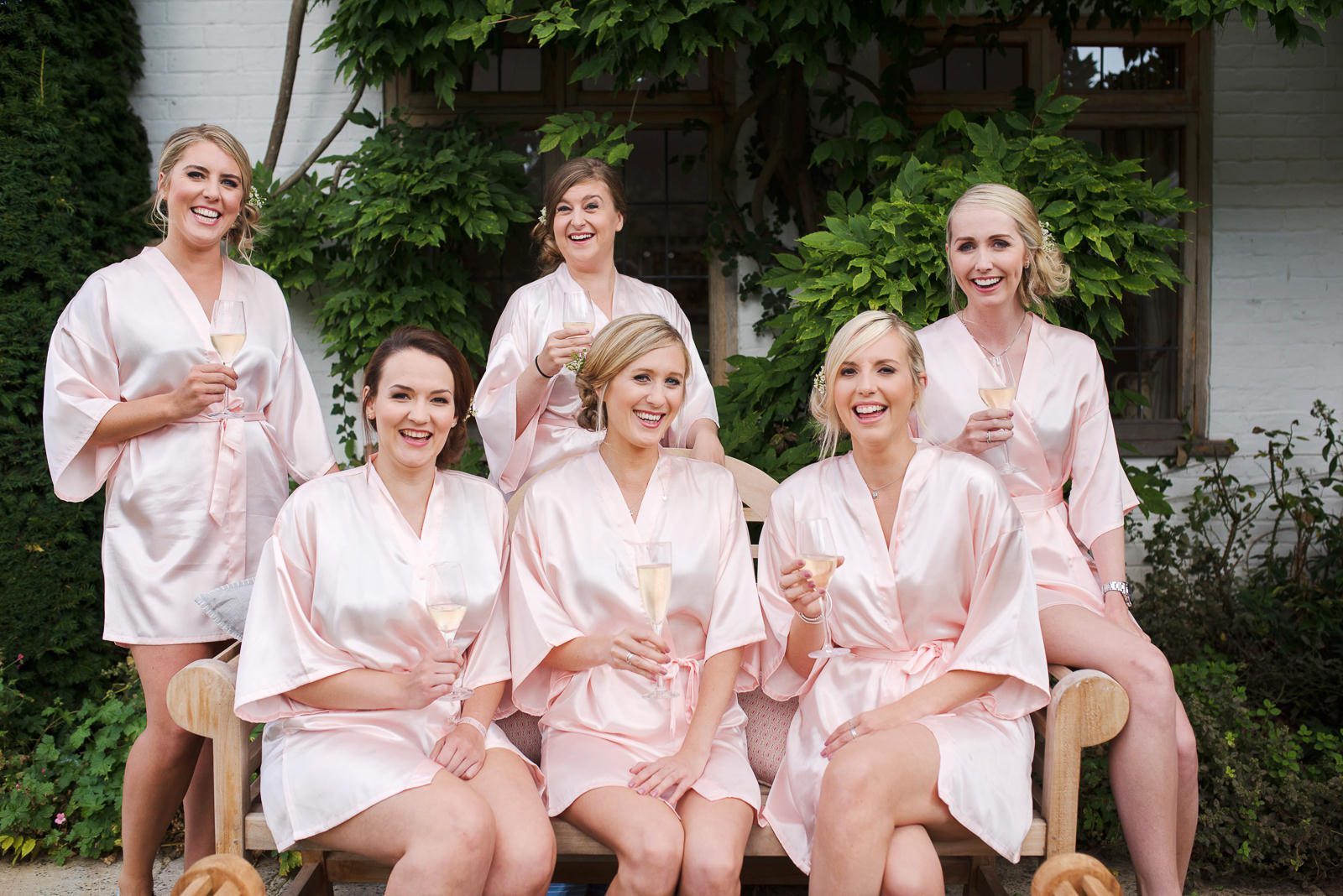 A stylish and fun photograph of the bridal party wearing pink satin dressing gowns and sipping Champagne.