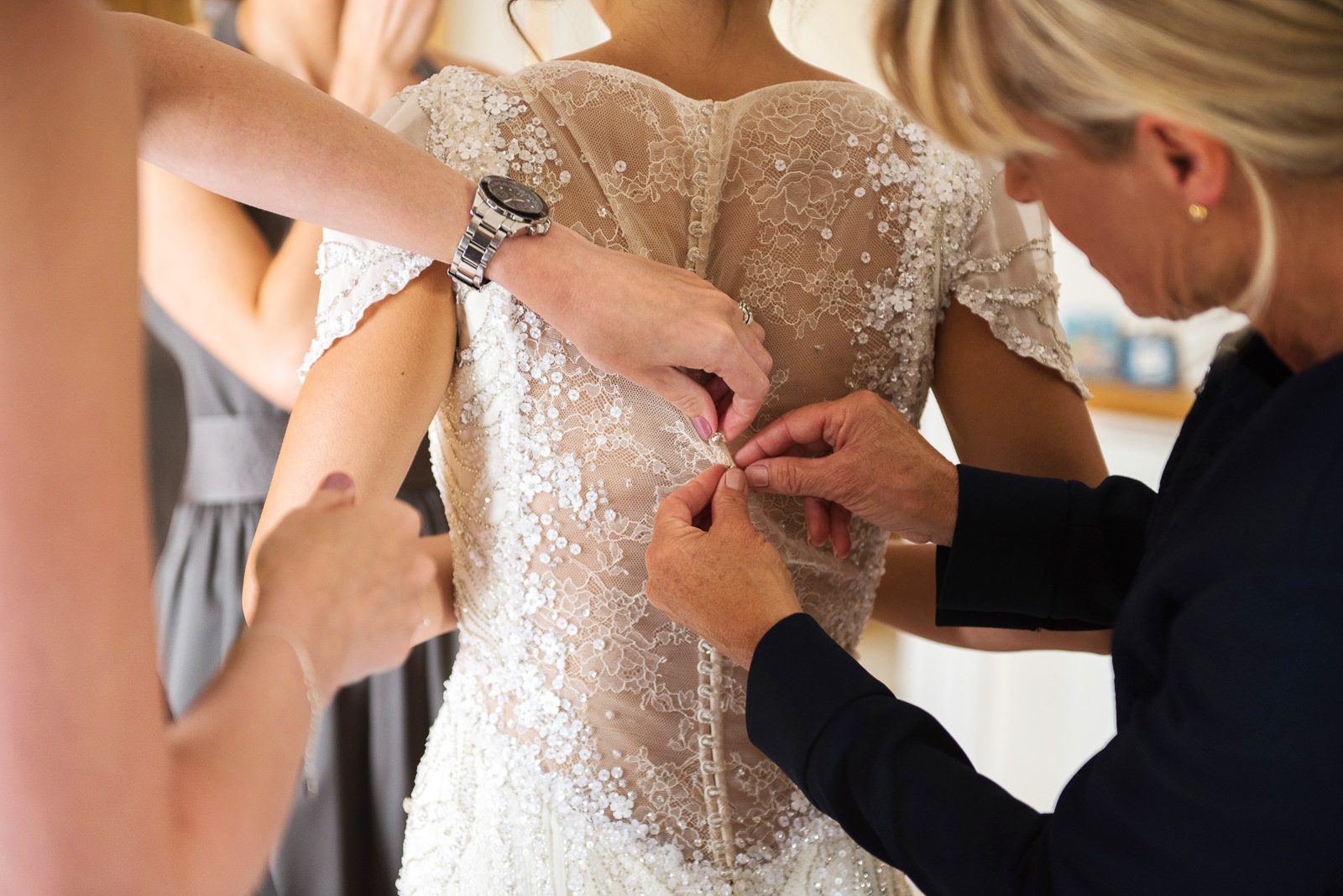 The brides mother does up the buttons of the back of her lace beaded Jenny Packham wedding dress.