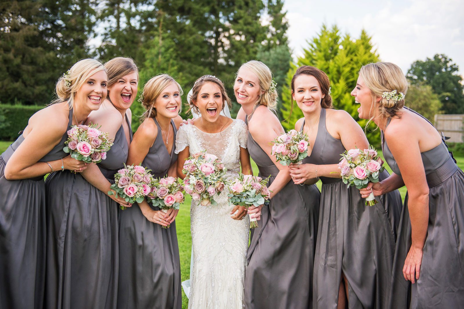 Stylish group shot of the bride and her bridesmaids wearing charcoal grey dresses and carrying pink bouquets..