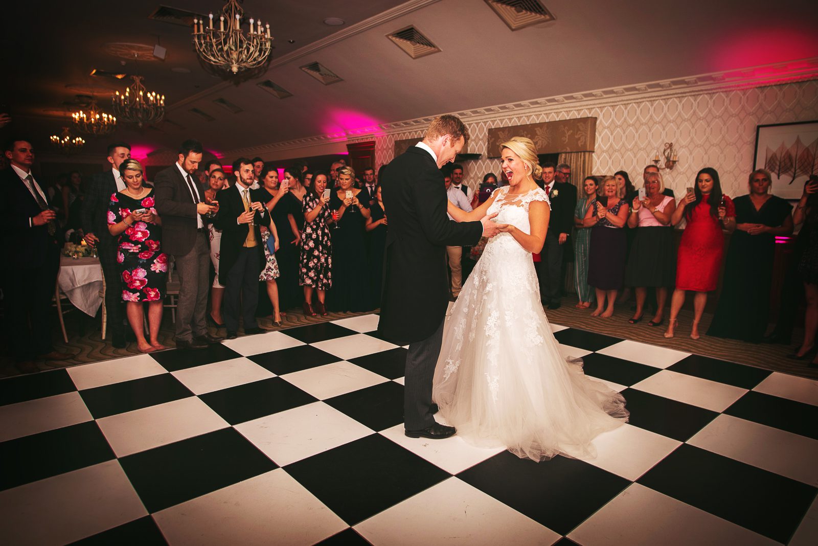 A bride and groom take their first dance on a chequered dance floor.